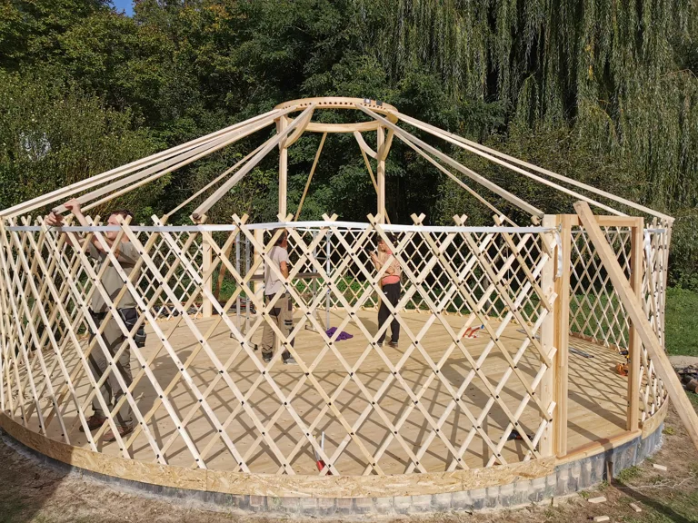 Yurt frame being built: golden-wood lattice wall and roof structure, work in progress