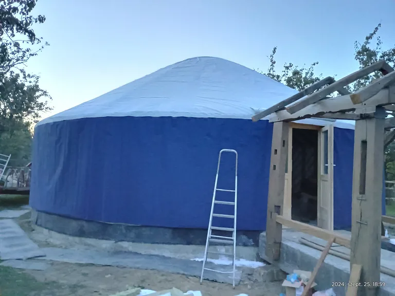 The finished yurt with blue covering, white roof and wooden entrance, at dusk