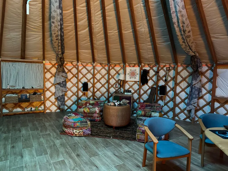 Cosy yurt interior: colourful kilim rug, floor cushions, a woven side table and blue armchairs in front of the lattice wall