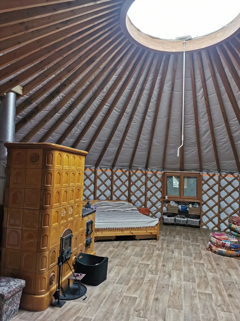 The warm interior of Barna's own yurt: the tiled stove glowing under the wooden crown ring and roof window, cold outside and warm inside