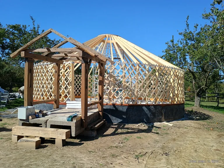 The full wooden frame of the 10-metre yurt on the deck, in sunshine under a blue sky