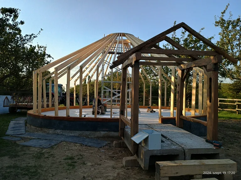 The golden wooden frame and covered entrance of the 10-metre yurt on the deck, in evening light