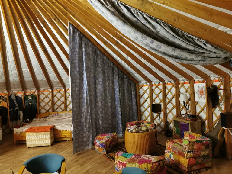 Zoned yurt interior: a curtain-separated bedroom, woven poufs and a kilim rug in the living area